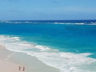 A photorealistic image of a beach event in Barbados where all the food and drinks are served in reusable or biodegradable containers. The vendors are using solar-powered equipment, and there are clearly marked recycling bins for different types of waste. Participants are actively using the recycling bins and are conscious of minimizing their environmental impact. The scene is set against the backdrop of a beautiful beach with clear blue water. Style: Environmental documentary photography with a focus on showcasing sustainable practices. Technical specs: 4K resolution, bright and cheerful lighting, vibrant color palette.